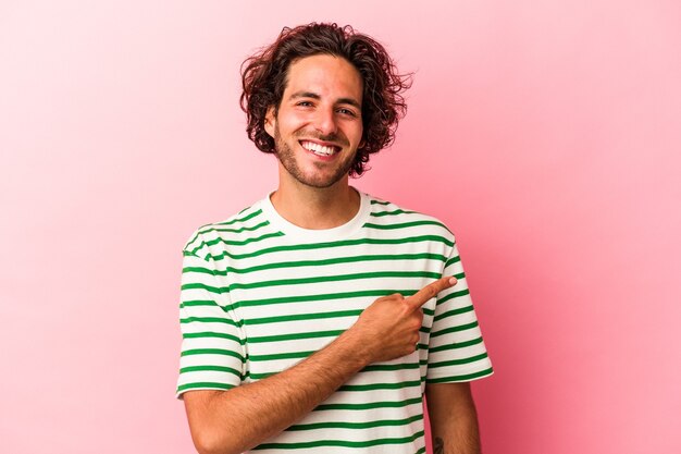 Jovem homem caucasiano isolado na rosa bakcground sorrindo e apontando de lado, mostrando algo no espaço em branco.