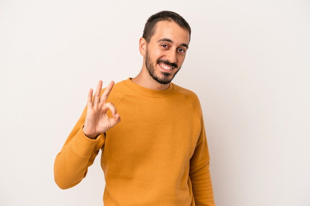 Jovem homem caucasiano isolado no fundo branco, alegre e confiante, mostrando um gesto de ok.