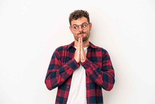 Jovem homem caucasiano isolado no fundo branco orando, mostrando devoção, pessoa religiosa em busca de inspiração divina.