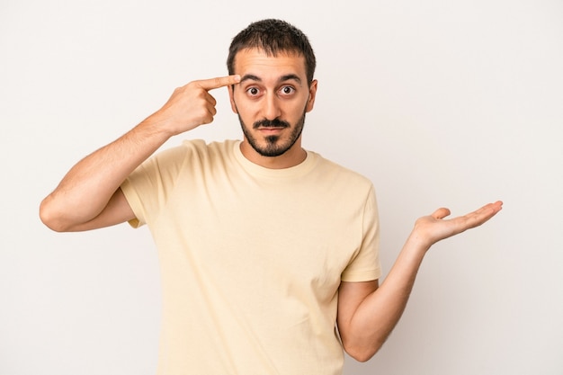 Jovem homem caucasiano isolado no fundo branco, segurando e mostrando um produto disponível.