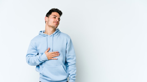 Jovem homem caucasiano isolado no fundo branco toca a barriga, sorri suavemente, comendo e o conceito de satisfação.