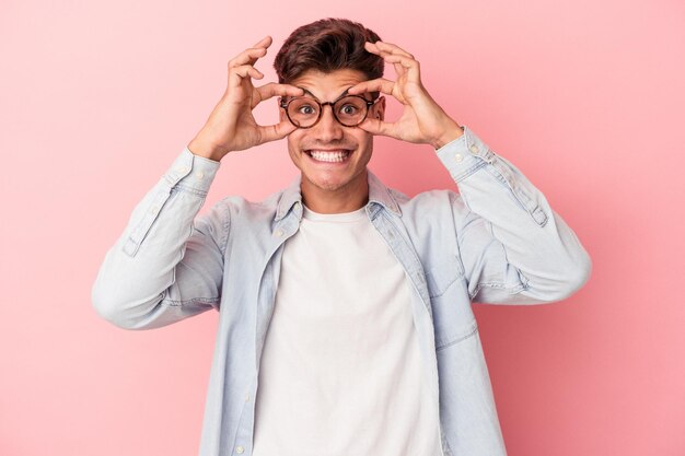 Jovem homem caucasiano isolado no fundo rosa, mantendo os olhos abertos para encontrar uma oportunidade de sucesso.