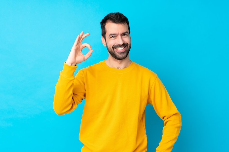 Foto jovem homem caucasiano isolado parede azul mostrando sinal okey com os dedos