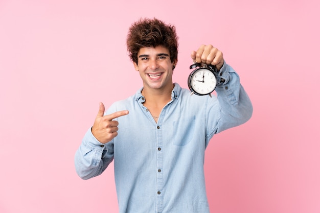 Jovem homem caucasiano isolado parede rosa segurando despertador vintage