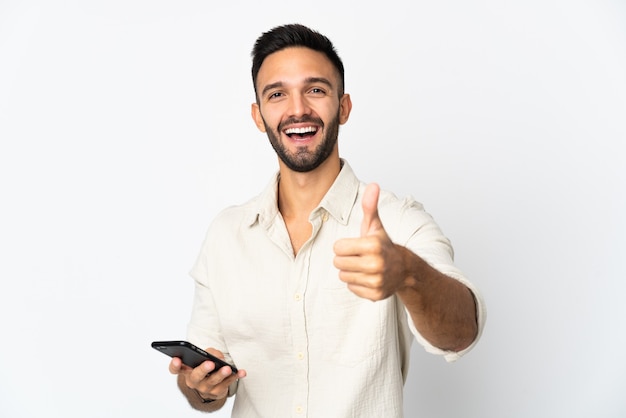 Jovem homem caucasiano isolado usando um telefone celular enquanto fazia o polegar para cima