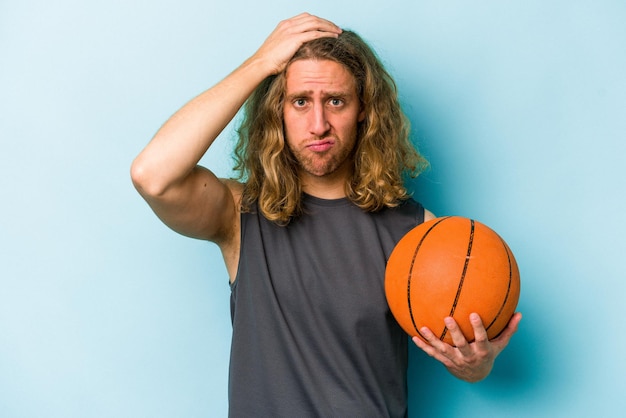 Jovem homem caucasiano jogando basquete isolado em fundo azul, chocado, ela se lembrou de uma reunião importante