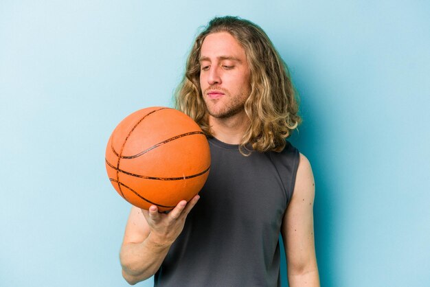 Jovem homem caucasiano jogando basquete isolado em fundo azul