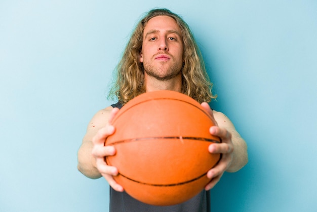 Jovem homem caucasiano jogando basquete isolado em fundo azul