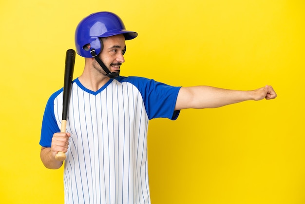 Jovem homem caucasiano jogando beisebol isolado em um fundo amarelo e fazendo um gesto de polegar para cima