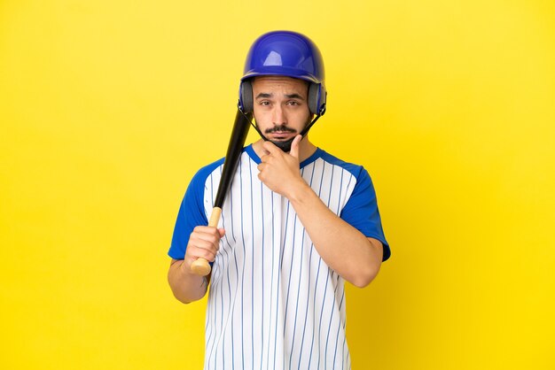 Jovem homem caucasiano jogando beisebol isolado em um fundo amarelo pensando