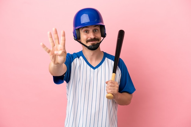 Jovem homem caucasiano jogando beisebol isolado em um fundo rosa feliz e contando quatro com os dedos