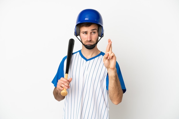 Jovem homem caucasiano jogando beisebol isolado no fundo branco, cruzando os dedos e desejando o melhor