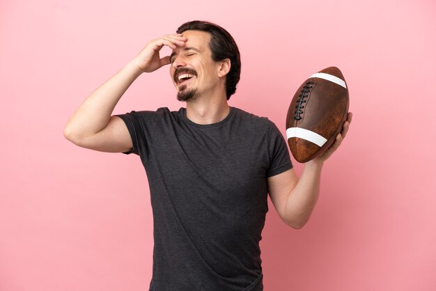 Foto jovem homem caucasiano jogando rugby isolado em um fundo rosa sorrindo muito