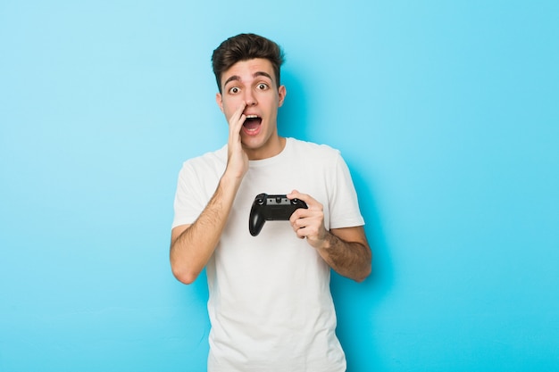 Jovem homem caucasiano jogando videogame com controlador de jogo gritando animado para a frente.