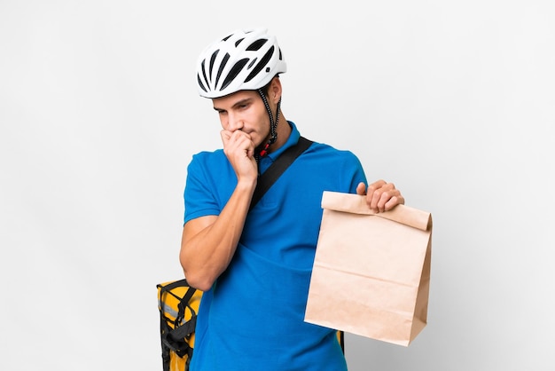 Foto jovem homem caucasiano levando um saco de comida para viagem sobre fundo isolado com dúvidas