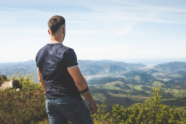 Jovem homem caucasiano no topo da montanha de Oiz, com vistas deslumbrantes sobre o verde País Basco.