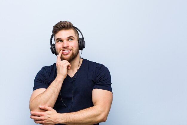 Jovem homem caucasiano ouvindo música relaxado pensando em algo olhando para um espaço de cópia.