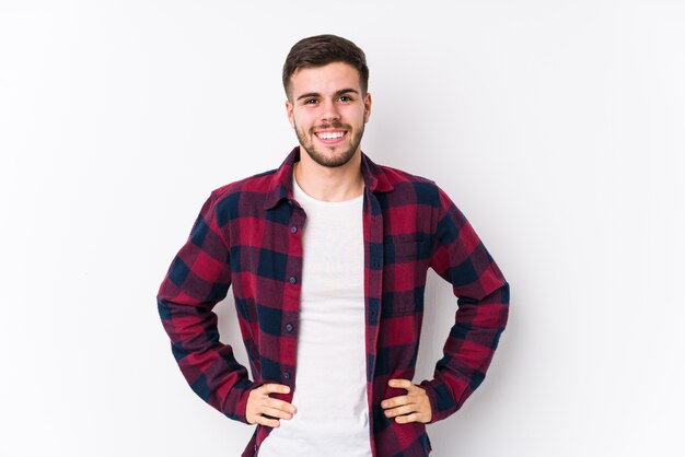 Jovem homem caucasiano posando em branco isolado confiante, mantendo as mãos nos quadris.