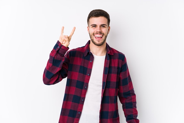 Jovem homem caucasiano posando em branco isolado, mostrando um gesto de chifres como um conceito de revolução.