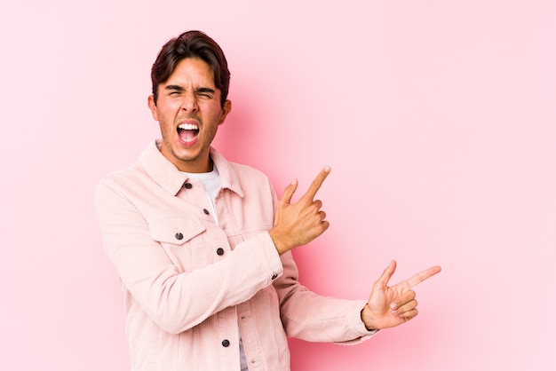 Jovem homem caucasiano posando em rosa isolado apontando com o dedo indicador para um espaço de cópia, expressando emoção e desejo.