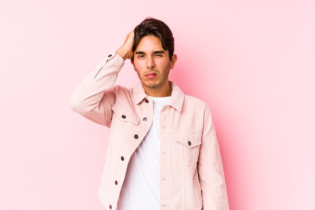 Jovem homem caucasiano posando em um rosa isolado cansado e com muito sono, mantendo a mão na cabeça.