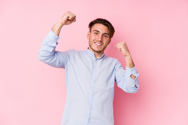 Jovem homem caucasiano posando em uma parede rosa isolada comemorando um dia especial, saltos e levante os braços com energia.