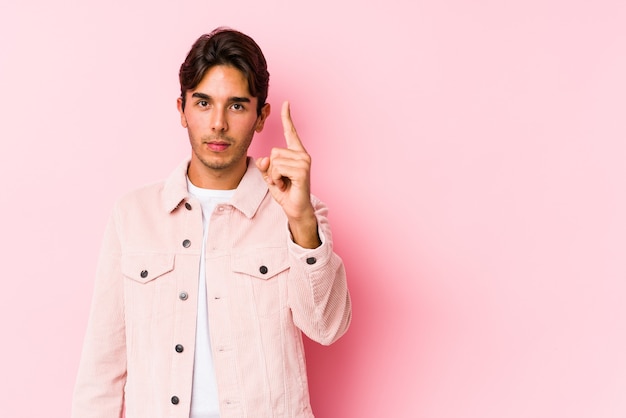 Jovem homem caucasiano posando em uma parede rosa isolada mostrando o número um com o dedo.