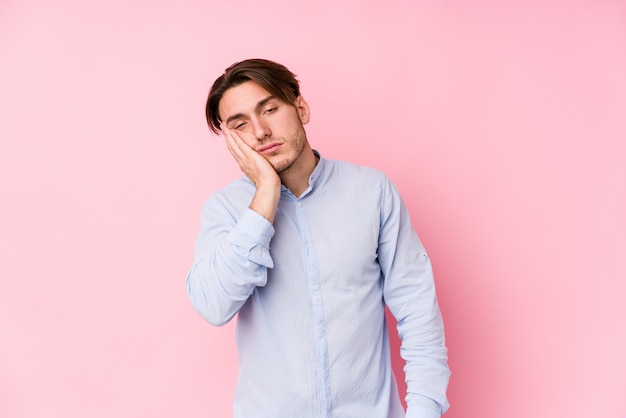 Jovem homem caucasiano posando em uma parede rosa isolada quem está entediado, cansado e precisa de um dia de relaxamento.