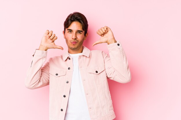 Jovem homem caucasiano posando em uma parede rosa isolada se sente orgulhoso e autoconfiante, exemplo a seguir.