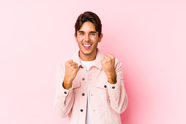 Jovem homem caucasiano posando em uma parede rosa isolada torcendo despreocupado e animado. Conceito de vitória.