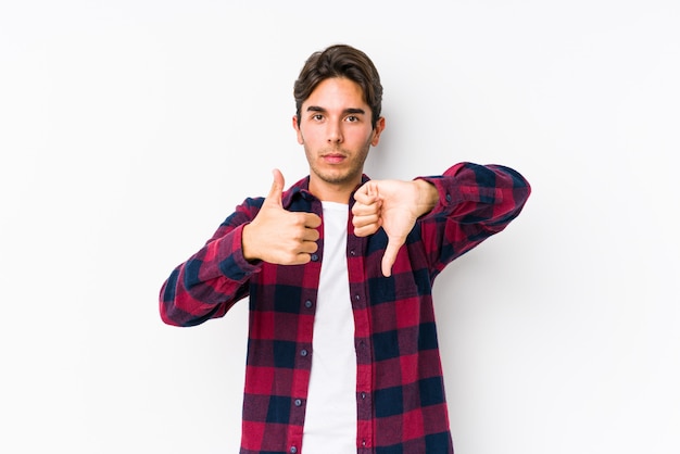 Jovem homem caucasiano posando em uma parede rosa, mostrando os polegares para cima e os polegares para baixo, difícil escolher o conceito