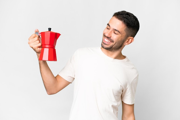 Jovem homem caucasiano segurando a cafeteira sobre fundo branco isolado com expressão feliz