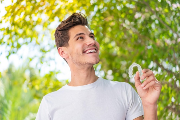 Jovem homem caucasiano segurando aparelho invisível ao ar livre olhando para cima enquanto sorri
