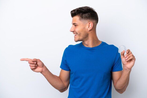 Jovem homem caucasiano segurando aparelho invisível isolado no fundo branco, apontando para o lado para apresentar um produto