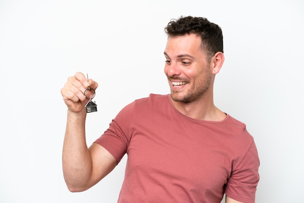 Foto jovem homem caucasiano segurando as chaves de casa isoladas no fundo branco com expressão feliz