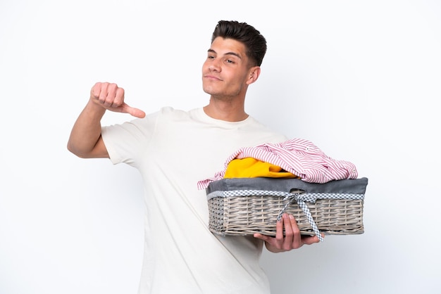 Jovem homem caucasiano segurando cesta de lavanderia isolada em fundo branco orgulhoso e satisfeito