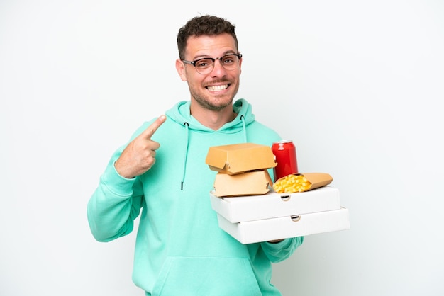 Foto jovem homem caucasiano segurando fast food isolado no fundo branco, dando um polegar para cima gesto