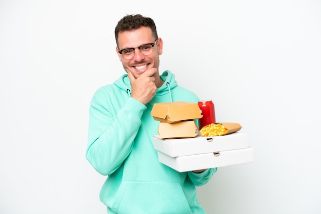 Jovem homem caucasiano segurando fast-food isolado no fundo branco feliz e sorridente