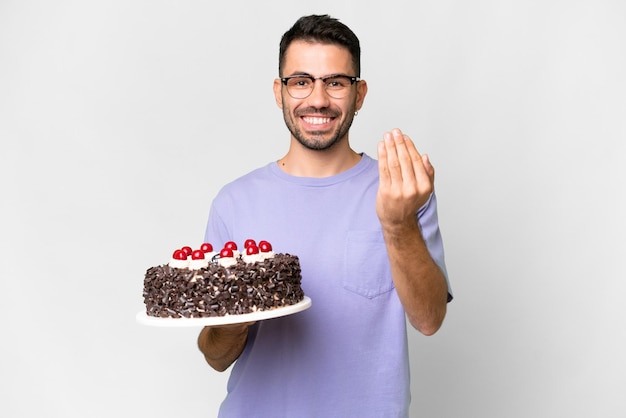 Jovem homem caucasiano segurando o bolo de aniversário isolado no fundo branco convidando para vir com a mão feliz que você veio