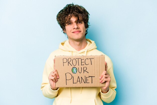 Jovem homem caucasiano segurando proteger nosso cartaz do planeta isolado em fundo azul