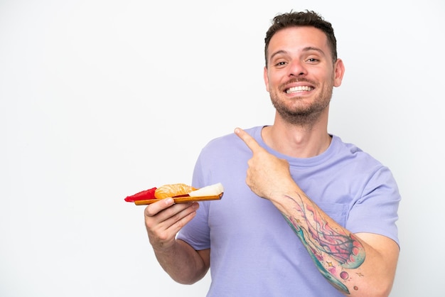 Jovem homem caucasiano segurando sashimi isolado no fundo branco apontando para trás