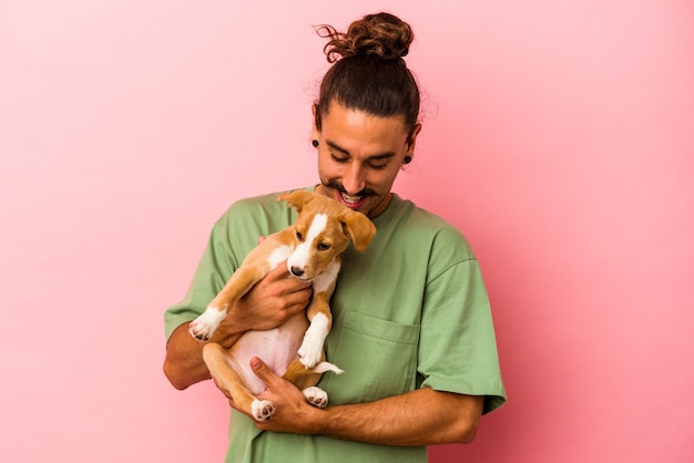 Jovem homem caucasiano segurando seu cachorrinho isolado em um fundo rosa