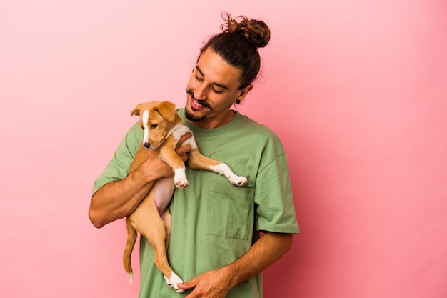 Jovem homem caucasiano segurando seu cachorrinho isolado em um fundo rosa