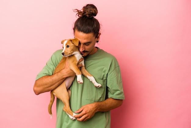 Foto jovem homem caucasiano segurando seu cachorrinho isolado em um fundo rosa