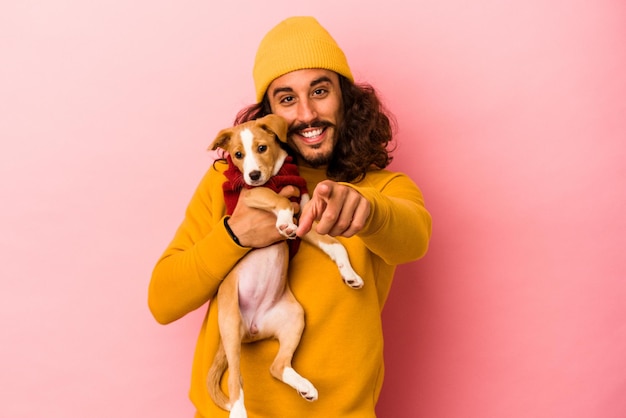 Foto jovem homem caucasiano segurando seu cachorrinho isolado em um fundo rosa