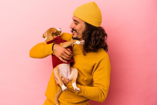 Jovem homem caucasiano segurando seu cachorrinho isolado em um fundo rosa
