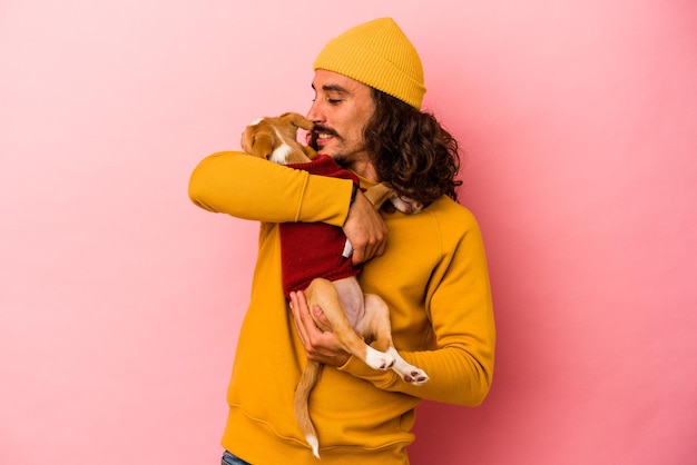 Jovem homem caucasiano segurando seu cachorrinho isolado em um fundo rosa