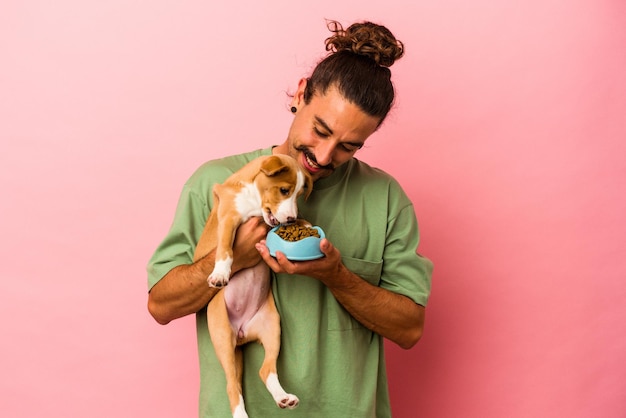 Foto jovem homem caucasiano segurando seu cachorro e sua comida isolada no fundo rosa