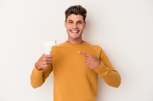 Jovem homem caucasiano segurando termômetro isolado no fundo branco, sorrindo e apontando de lado, mostrando algo no espaço em branco.