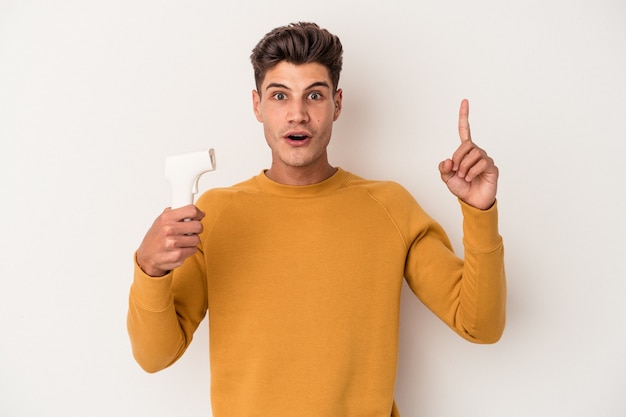 Jovem homem caucasiano segurando termômetro isolado no fundo branco, tendo uma ideia, o conceito de inspiração.